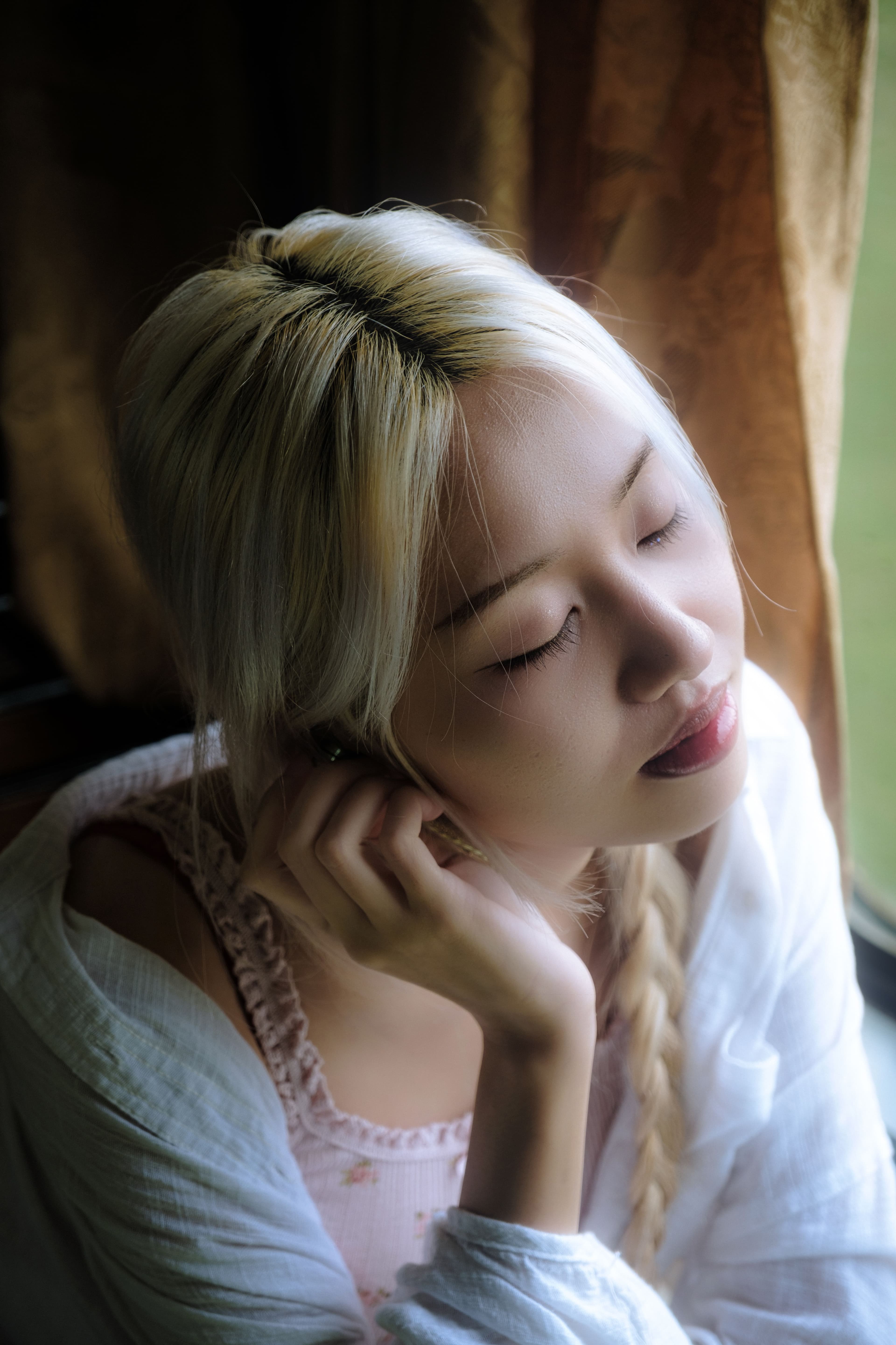 Woman sitting thoughtfully beside a bright window